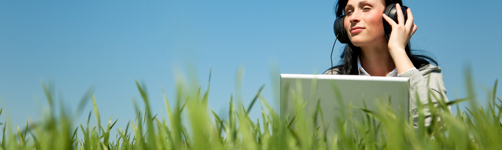 Frau hört mit Laptop im Gras Musik